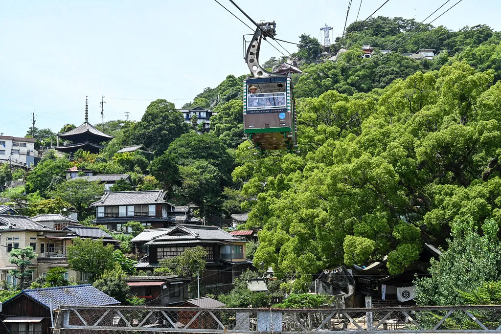 Kabina lanovky nad střechami a zeleným svahem Onomichi.