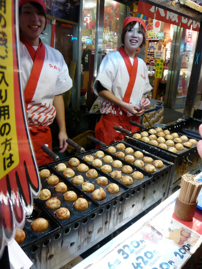 Cocineros que preparan takoyaki en comillas moldeadas en Osaka.