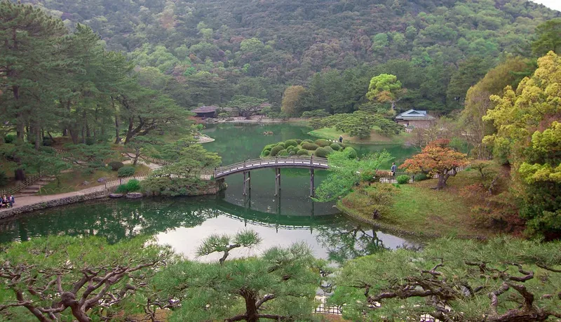 An arched bridge and pine trees beside a pond at Ritsurin Garden.