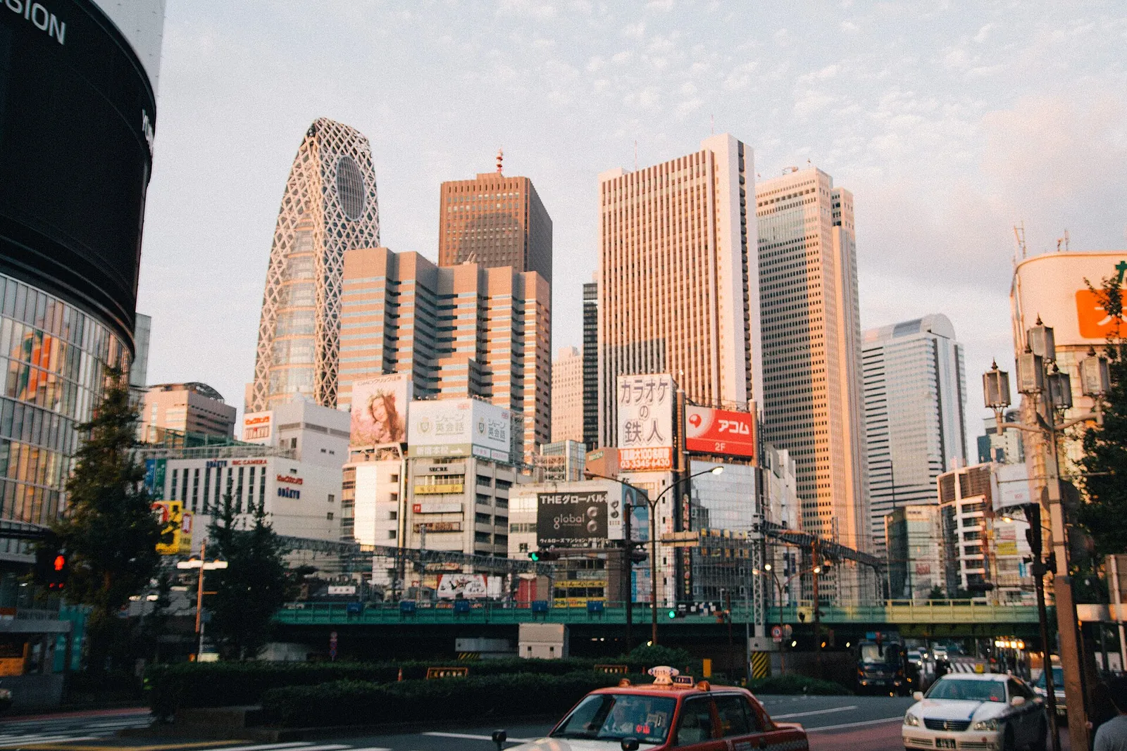 I grattacieli di Nishi-Shinjuku, tra cui la Mode Gakuen Cocoon Tower curva, visti da una strada trafficata con taxi e semafori