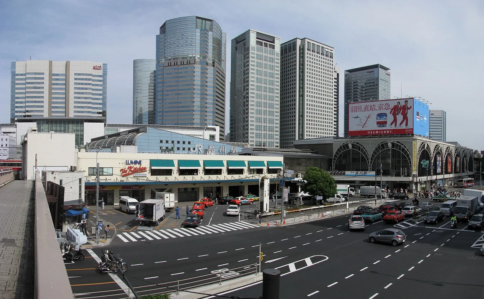 L'edificio basso d'ingresso della stazione di Shinagawa visto da una strada larga, con torri di uffici sullo sfondo