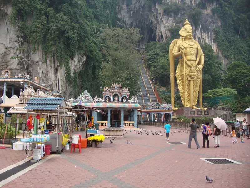 Golden Murugan statue and temple entrance below the limestone cliffs at Batu Caves