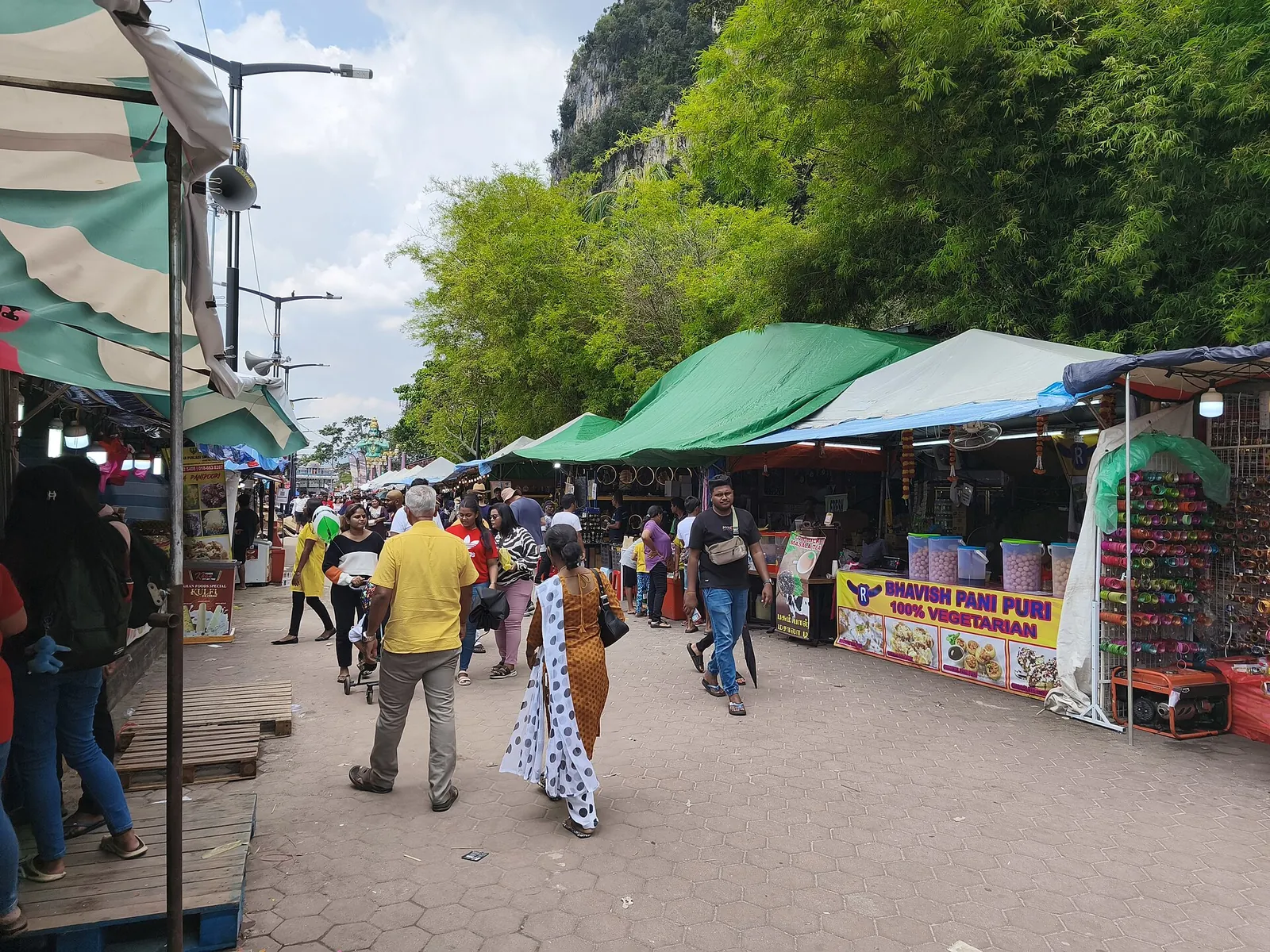 Visitors walking past vegetarian food stalls beneath the Batu Caves cliffs