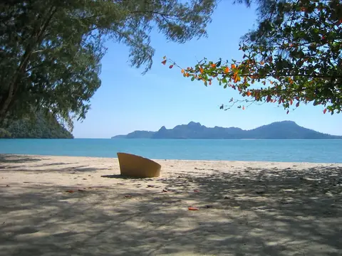 Prázdné sedadlo hledí z pláže Langkawi na moře a zalesněné ostrovy.