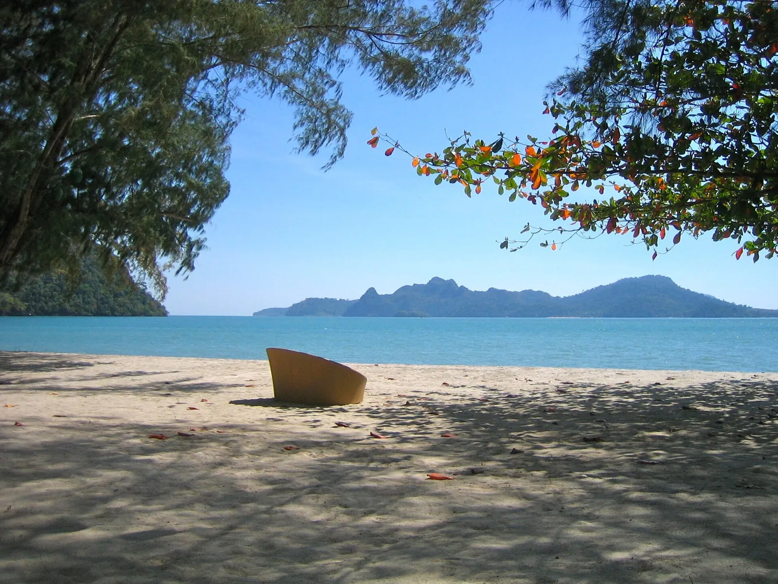 A shaded seat on sand facing the sea and distant Langkawi islands