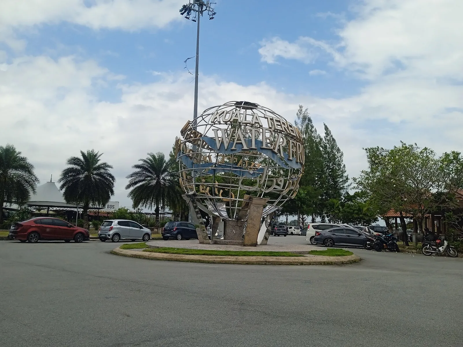 A waterfront globe sculpture beside palms and parked cars in Kuala Terengganu