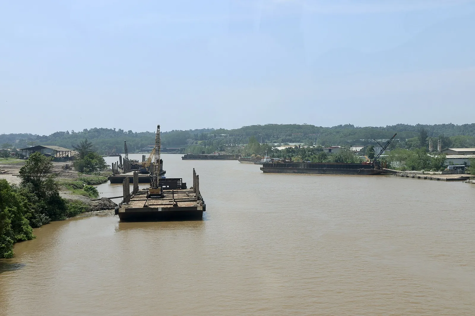 Broad muddy river with boats and a wooded opposite bank at Bintulu