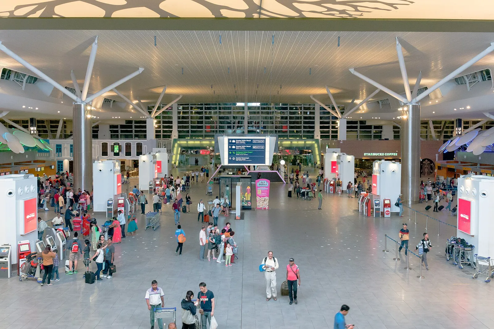 Travellers and check-in islands beneath the bright branching roof in KLIA2