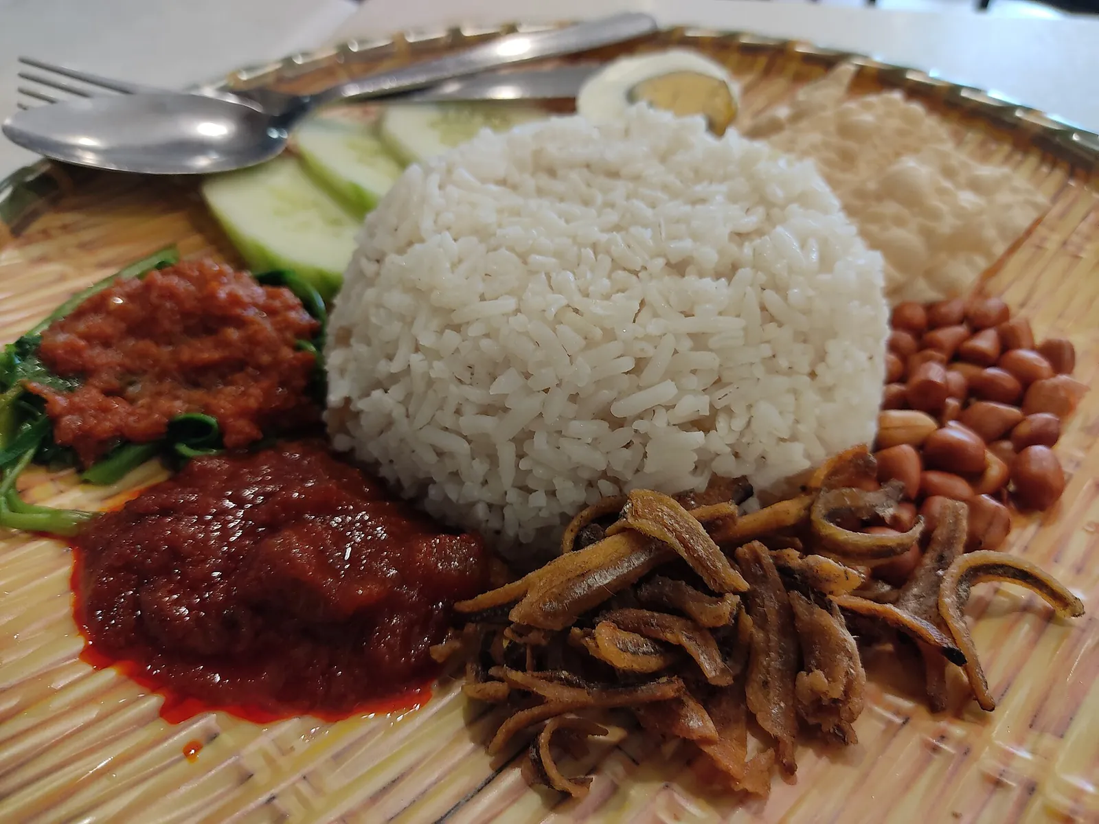 Nasi lemak with white rice, anchovies, peanuts, sambal and greens on a plate