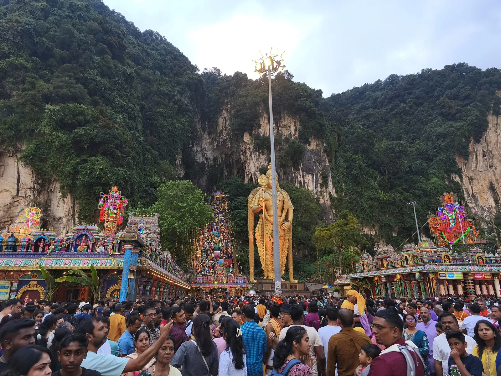 Davy věřících pod zlatou sochou Murugana a vápencovými útesy Batu Caves při Thaipusamu