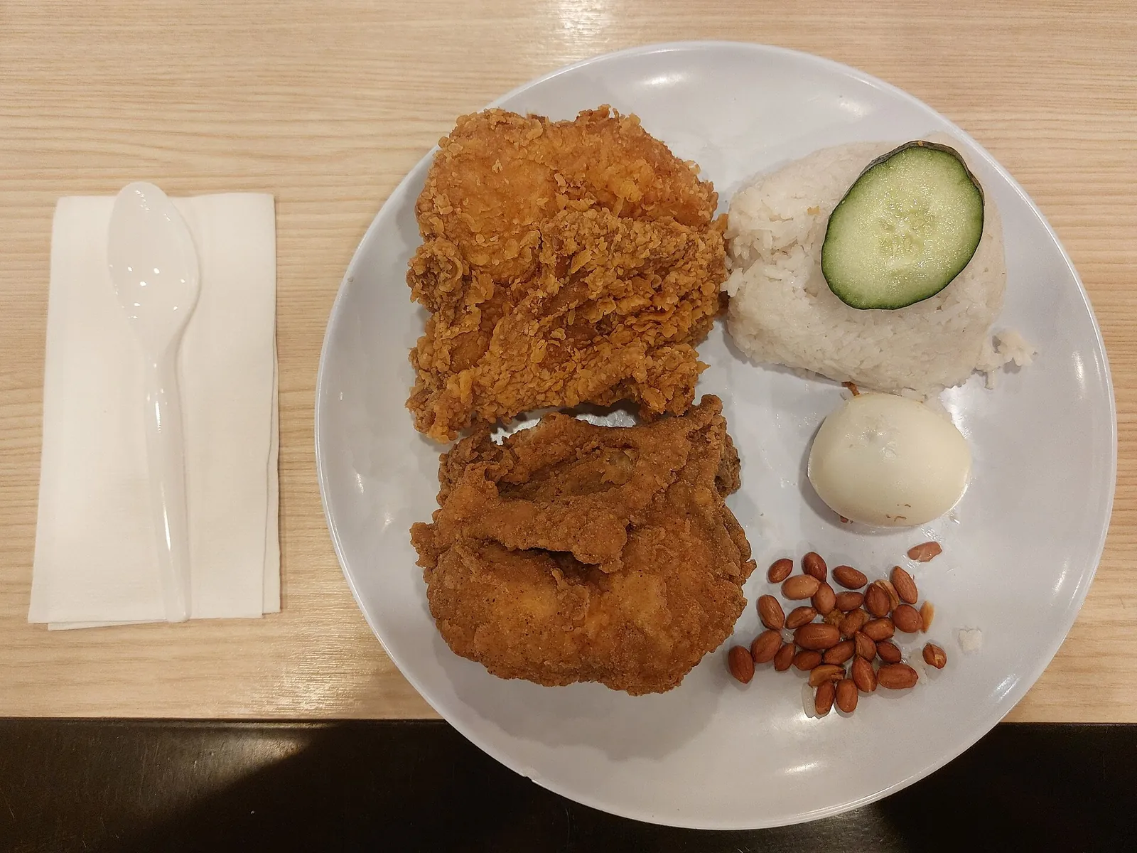 Nasi lemak with fried chicken, rice, egg, cucumber and peanuts on a white plate