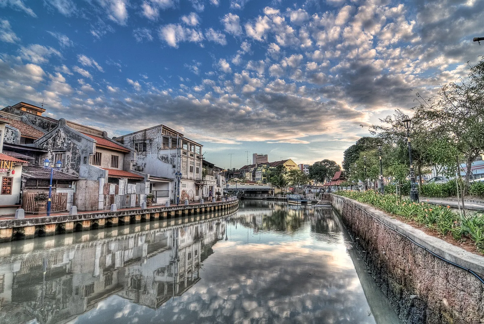 Clouds and riverside buildings reflected in the Melaka River at sunrise