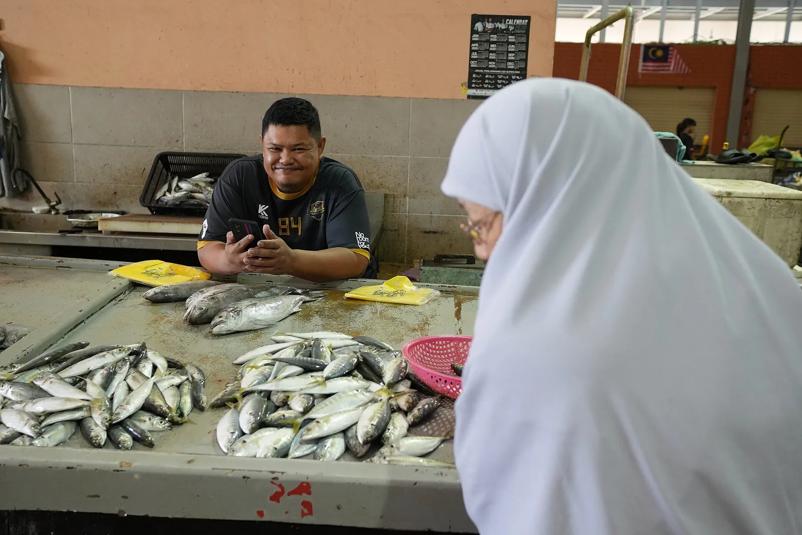 Fishmonger and customer beside displayed fish at Payang Market in Kuala Terengganu