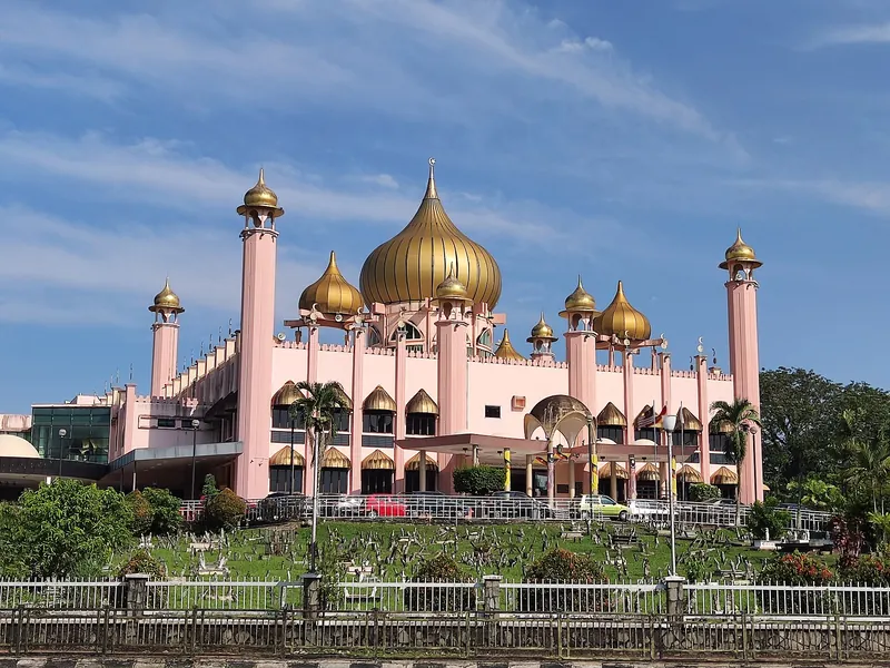Pink walls and golden domes of Kuching City Mosque beneath a blue sky