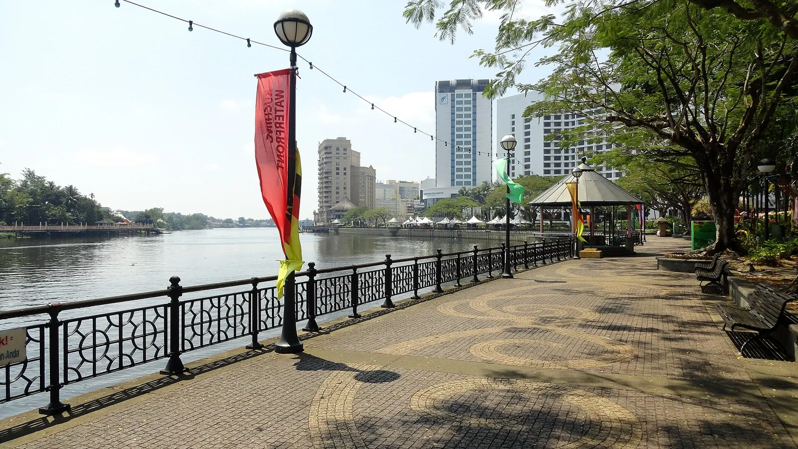 A paved riverside promenade and trees along the Kuching waterfront