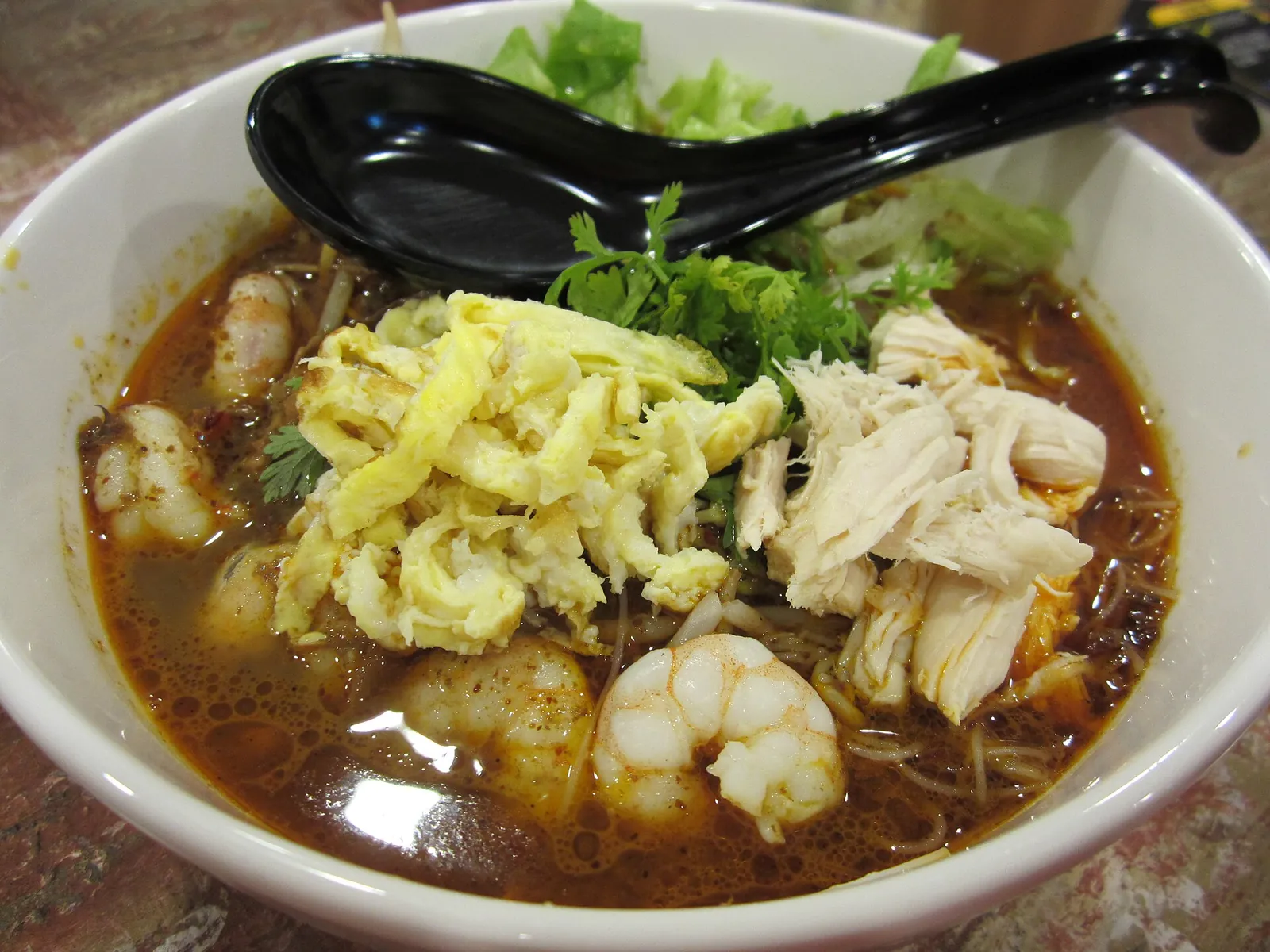 A bowl of Sarawak laksa topped with egg, prawns and shredded meat