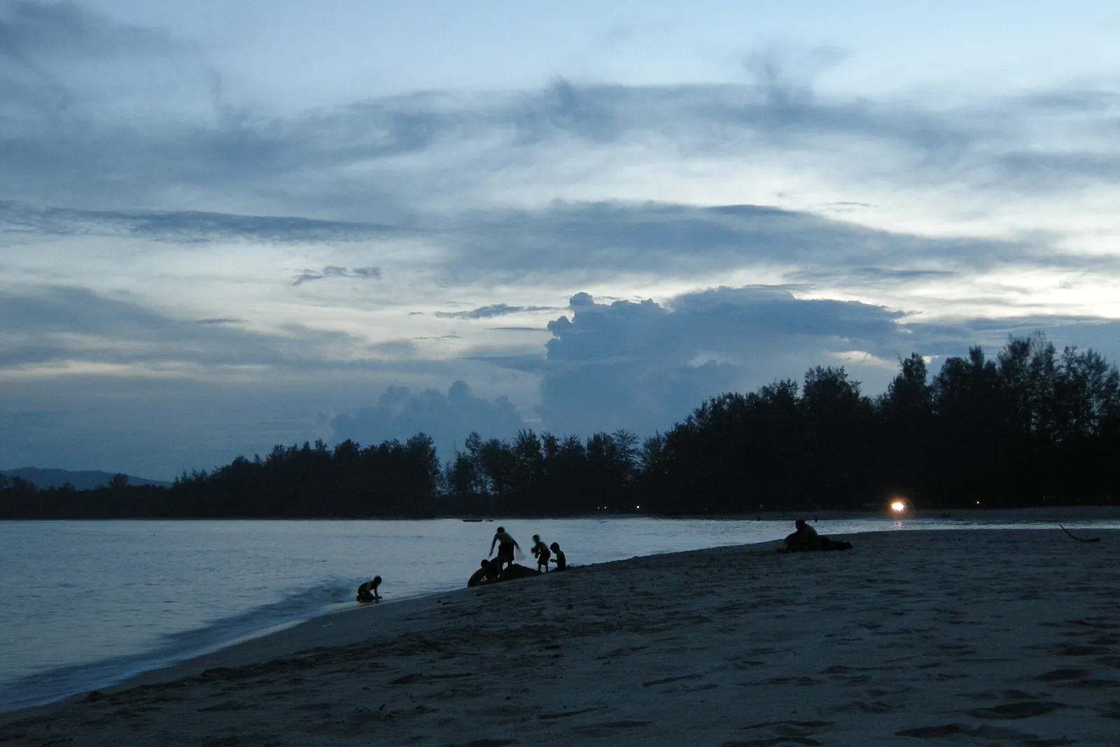 People on the Cherating shoreline under a fading evening sky