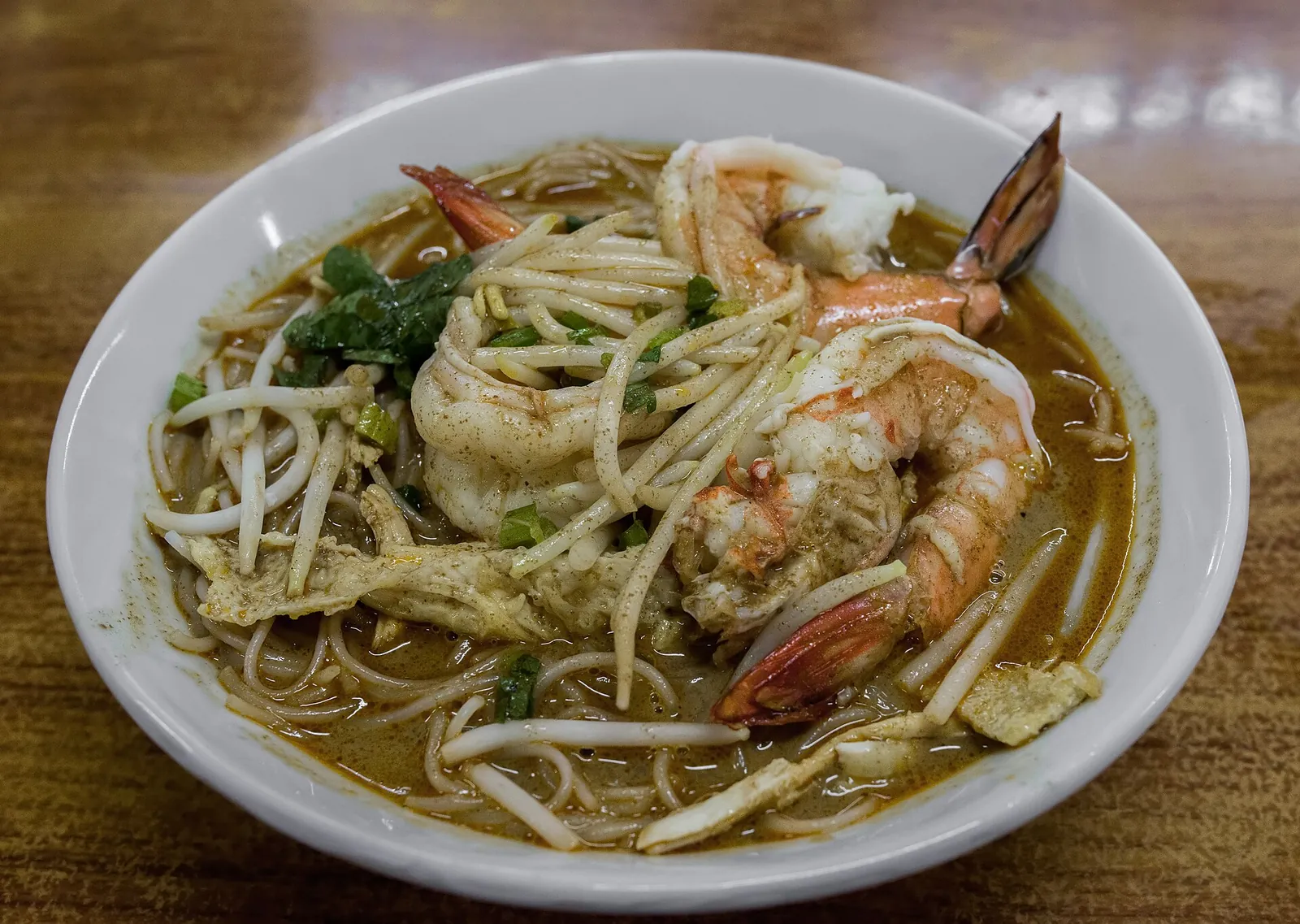 Laksa noodles topped with prawns and bean sprouts in a ceramic bowl