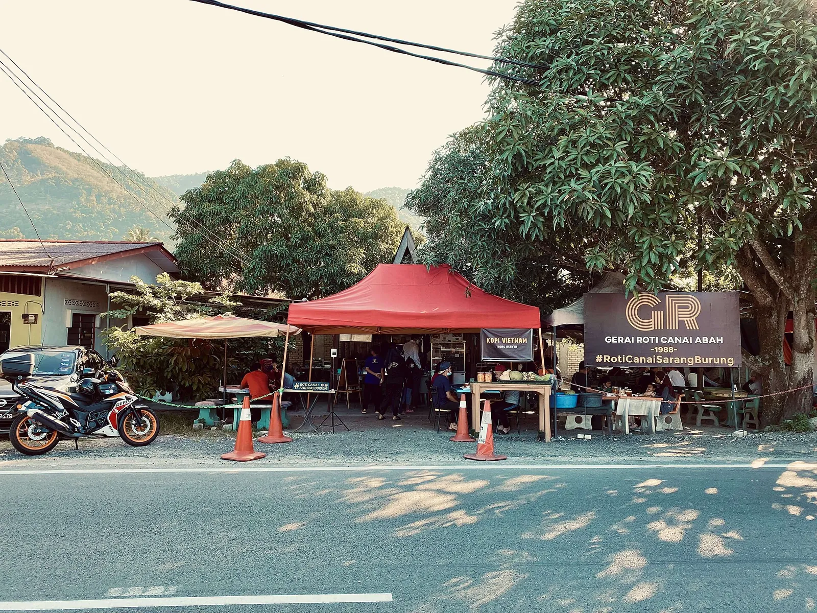 Outdoor restaurant tents and a roti canai sign beside a road in Sungai Rusa
