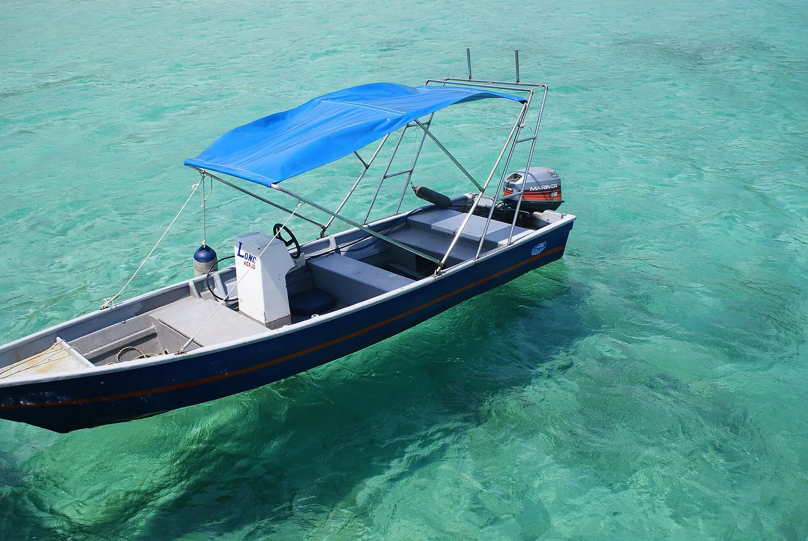 A small covered boat floating in clear green water at Salang on Tioman Island