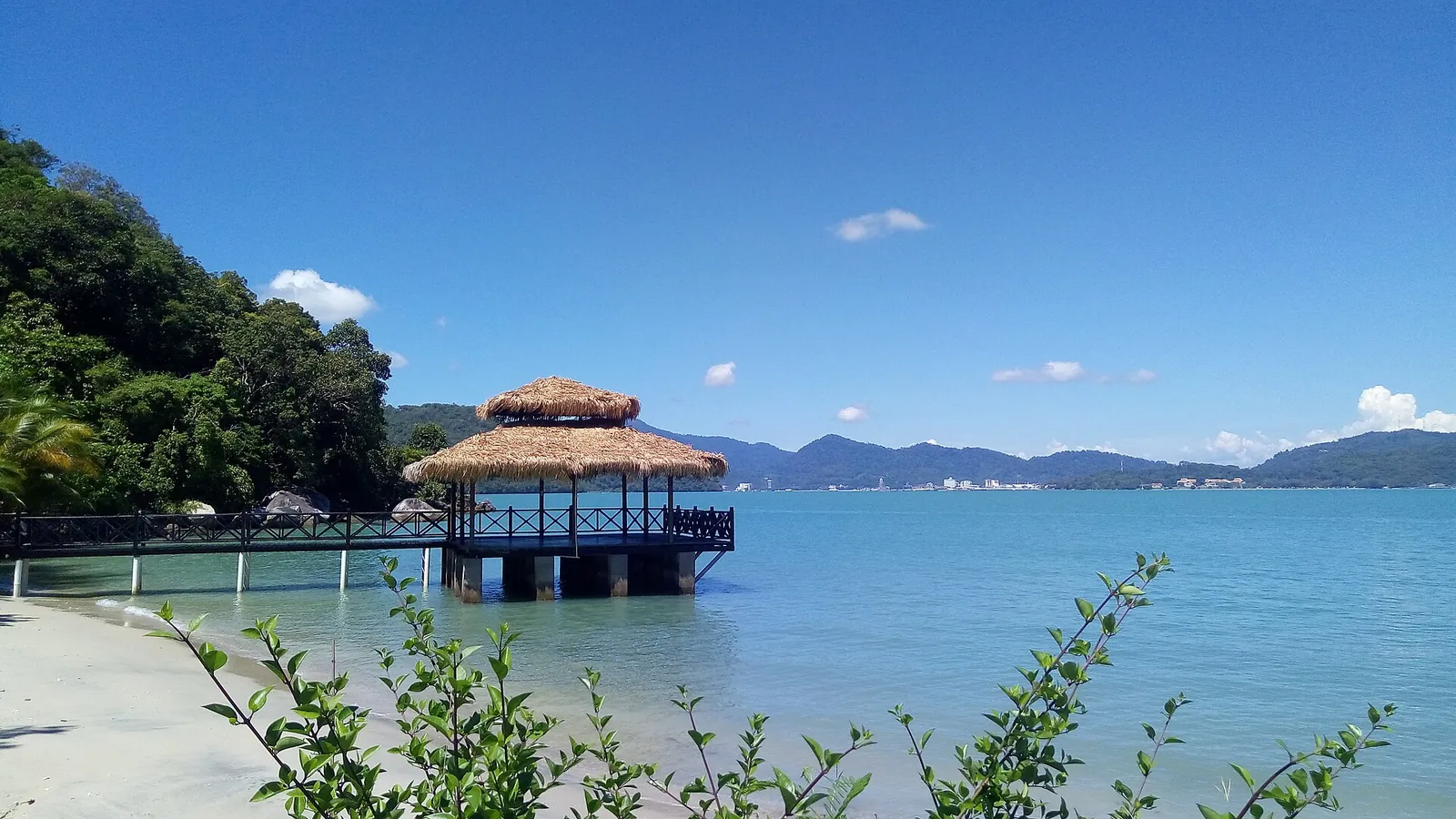 Malý pavilon hledí na modrou vodu a zalesněné ostrovy na Pulau Tuba v souostroví Langkawi.