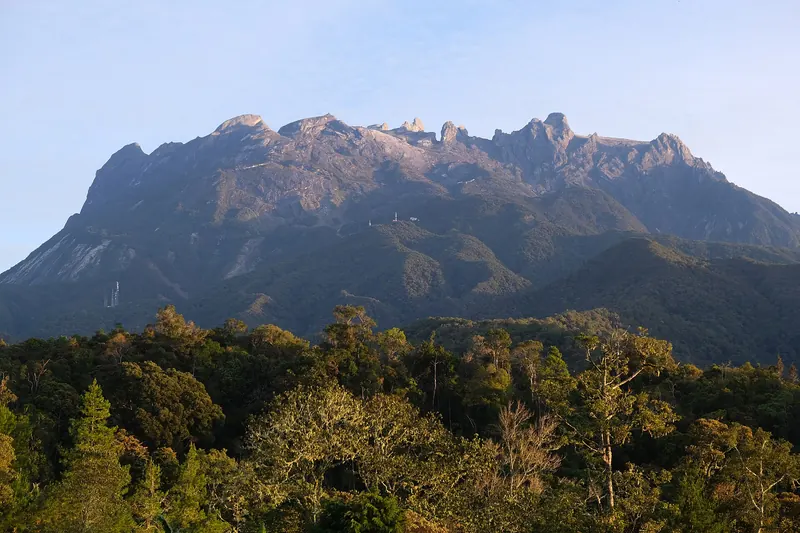 Sunlit Mount Kinabalu above green vegetation viewed from Kampong Kundasang