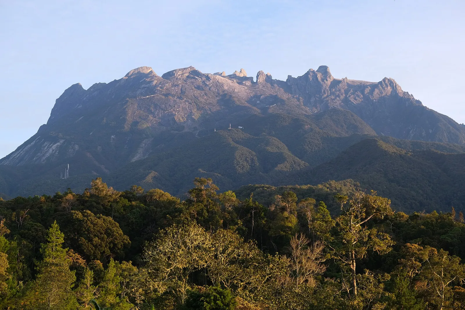 Sunlit Mount Kinabalu above green vegetation viewed from Kampong Kundasang