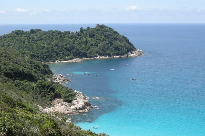 Bright turquoise water beside a forested headland in the Perhentian Islands