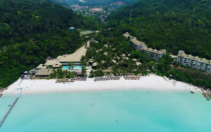 Turquoise water and white sand beside green hills on Redang Island