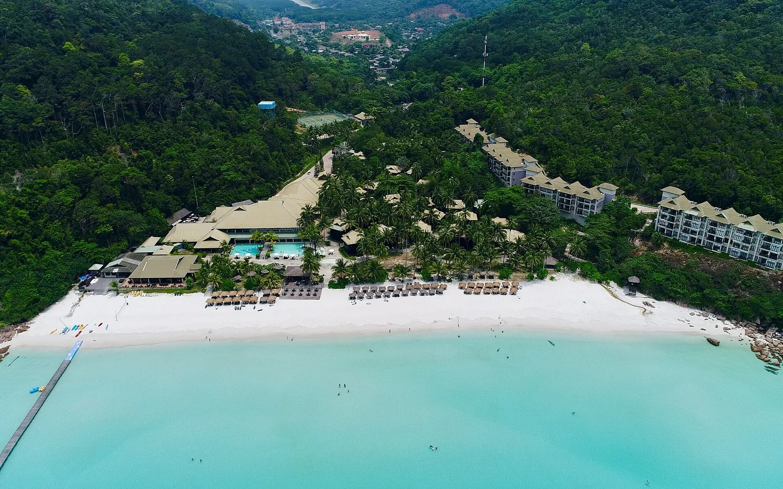 Turquoise water and white sand beside green hills on Redang Island
