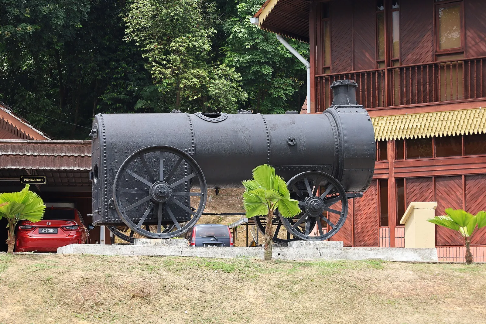 Historic steam engine displayed beside a wooden building at the Negeri Sembilan State Museum