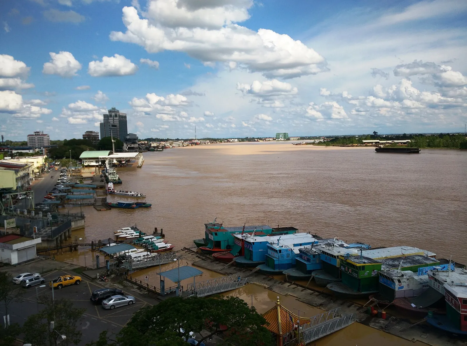Boats beside the broad Rajang River and Sibu waterfront under a blue sky