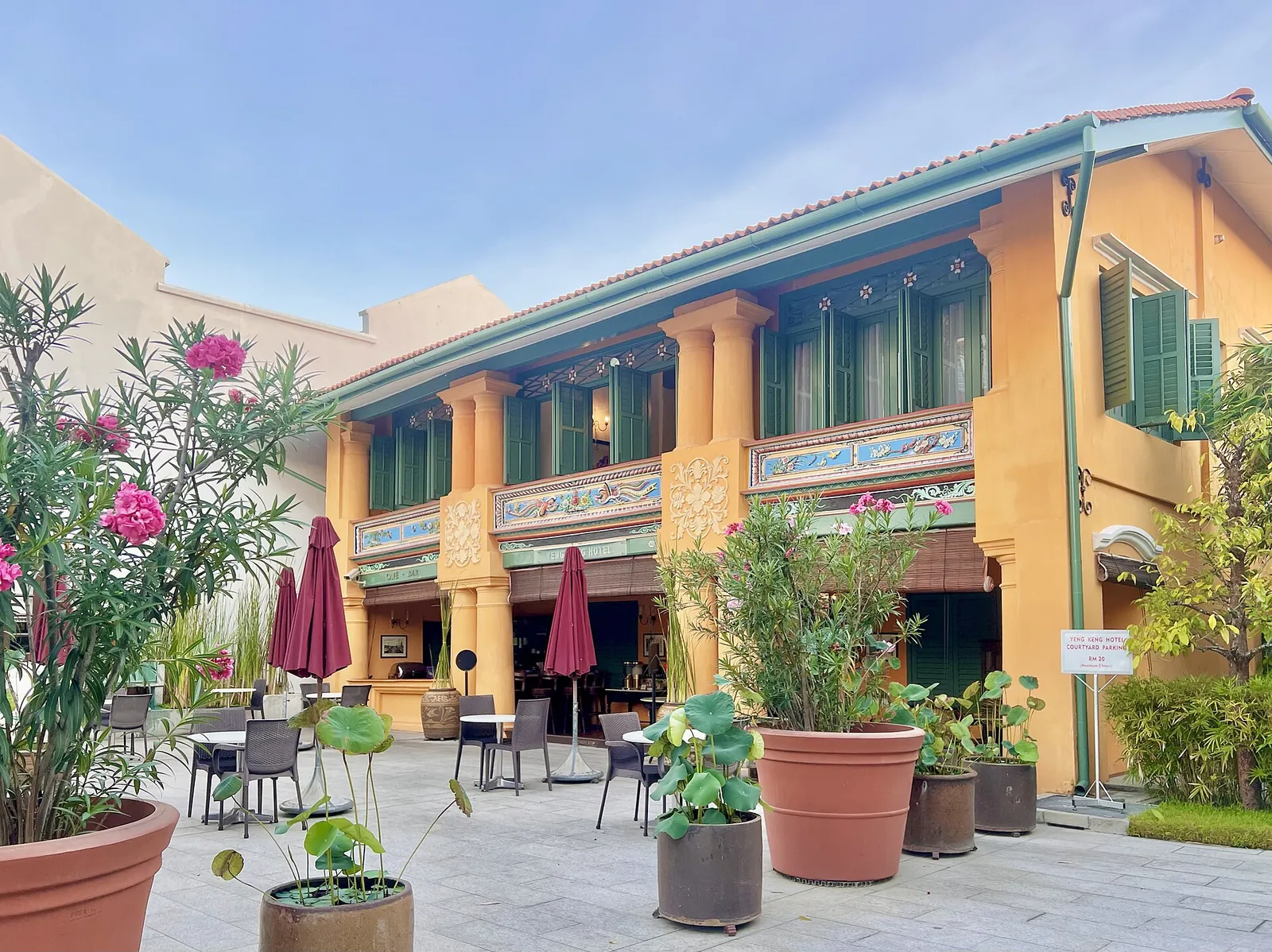 Sunlit yellow heritage hotel facade and red parasols around a courtyard in George Town