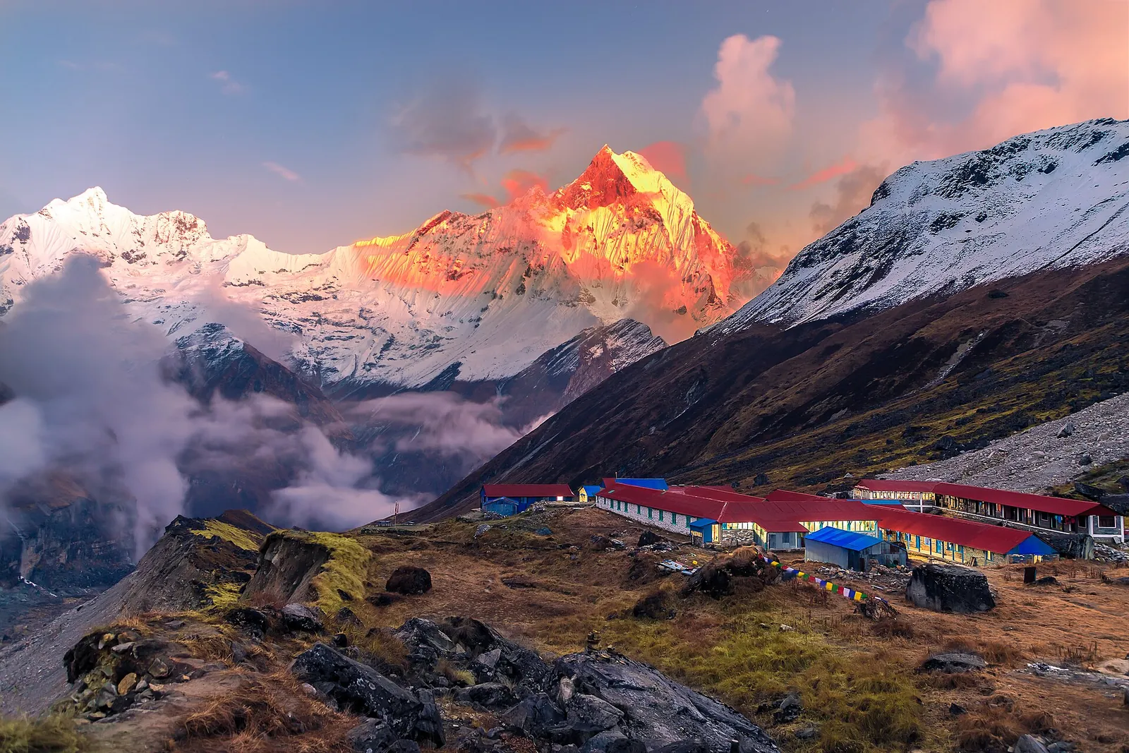Luz rojiza del atardecer sobre el pico Cola de Pez, por encima de los alojamientos de tejados azules del campo base del Annapurna