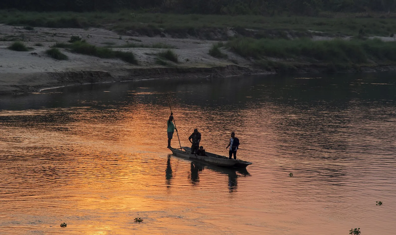 Una piccola barca con passeggeri attraversa il fiume Rapti al tramonto a Sauraha