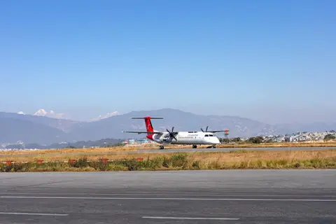 Un Dash 8 de dos hélices de Shree Airlines en tierra en el aeropuerto internacional Tribhuvan, con colinas y una línea de nieve al fondo
