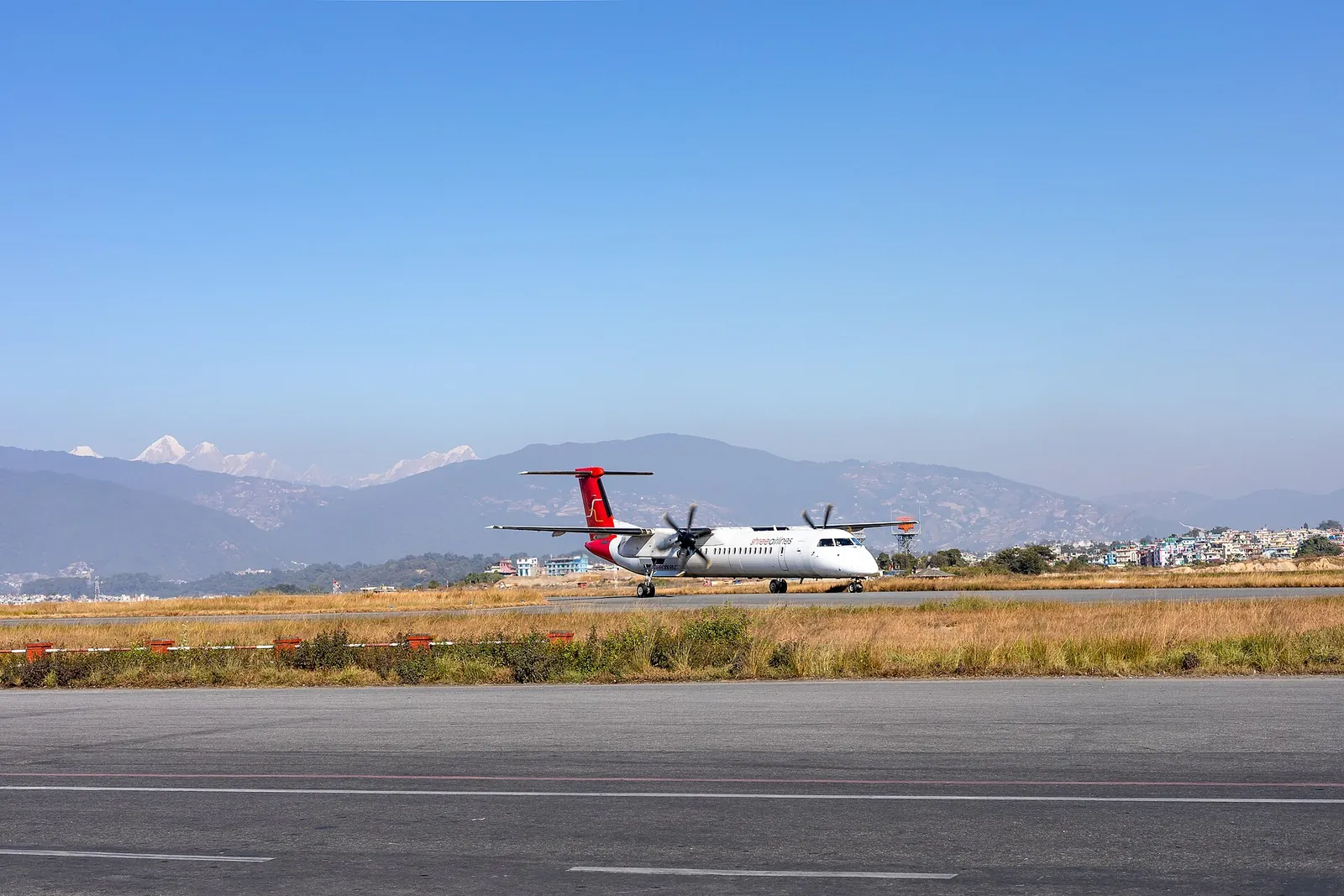 Dvoumotorový turbovrtulový Dash 8 společnosti Shree Airlines na ploše mezinárodního letiště Tribhuvan s kopci a sněhovou hranicí v pozadí