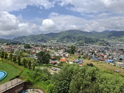 El valle de Katmandú visto desde una colina, con viviendas extendidas por el fondo del valle y colinas verdes bajo nubes dispersas
