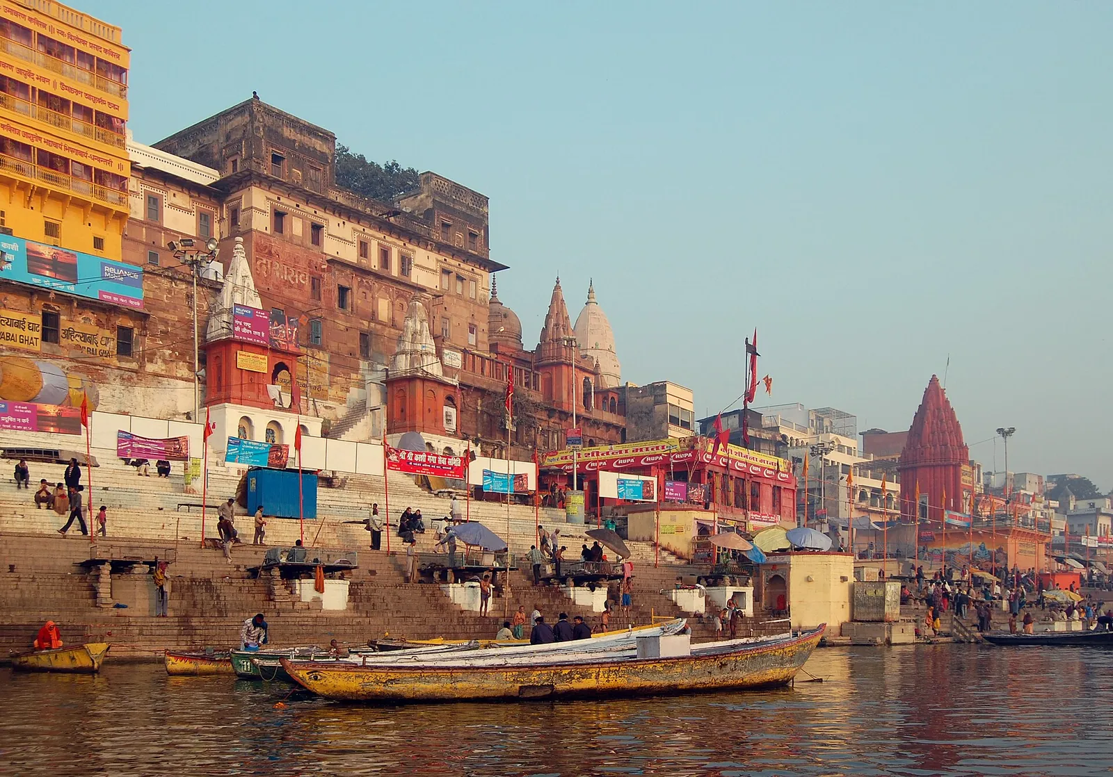 Temples and old buildings rising above the stone steps of Ahilyabai Ghat, with wooden boats moored on the Ganges