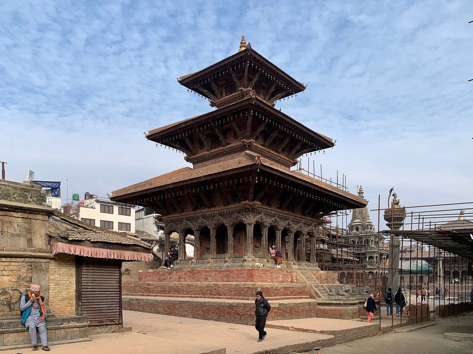 A three-tiered pagoda temple on a brick plinth in Patan Durbar Square under a blue sky