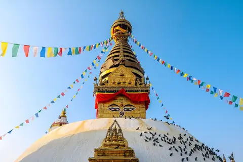 Estupa de Swayambhunath con aguja dorada, ojos pintados y banderas de oración contra un cielo azul