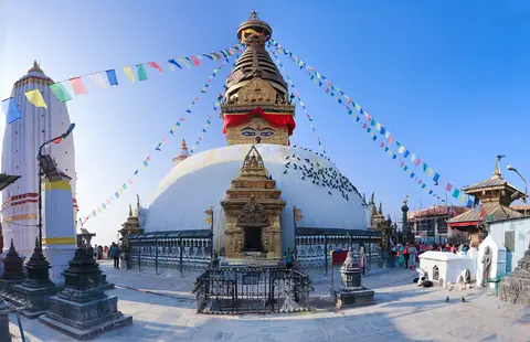 La cúpula blanca y la aguja dorada de la estupa de Swayambhunath con banderas de oración bajo un cielo azul