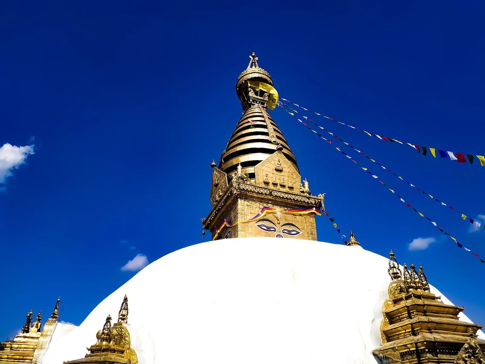 Aguja dorada y cúpula blanca de la estupa de Swayambhunath bajo un cielo azul intenso con banderas de oración