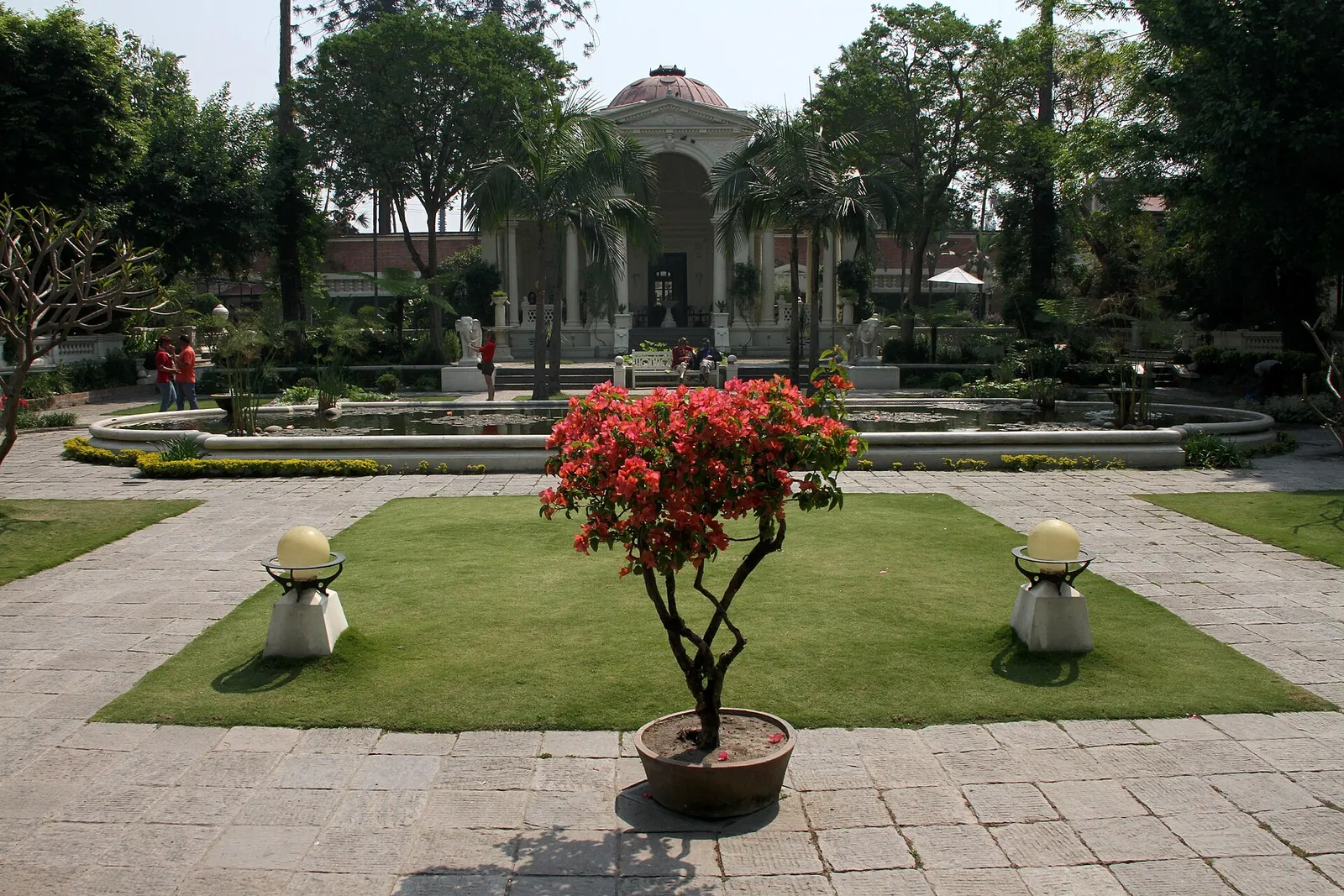 Jardín de los Sueños, Katmandú: un césped con un arbusto en flor y un pabellón entre árboles