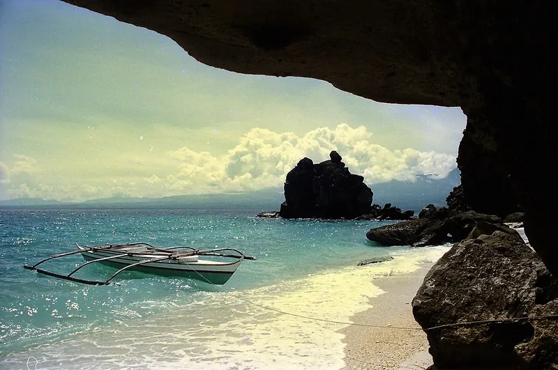 Outrigger boat and turquoise water seen beneath a rocky overhang on Apo Island