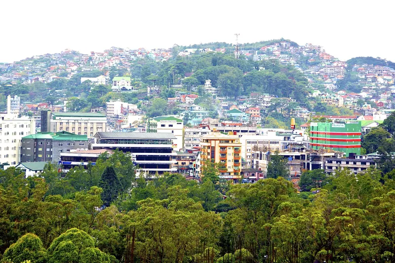 Baguio buildings spread over a green hillside beyond foreground trees
