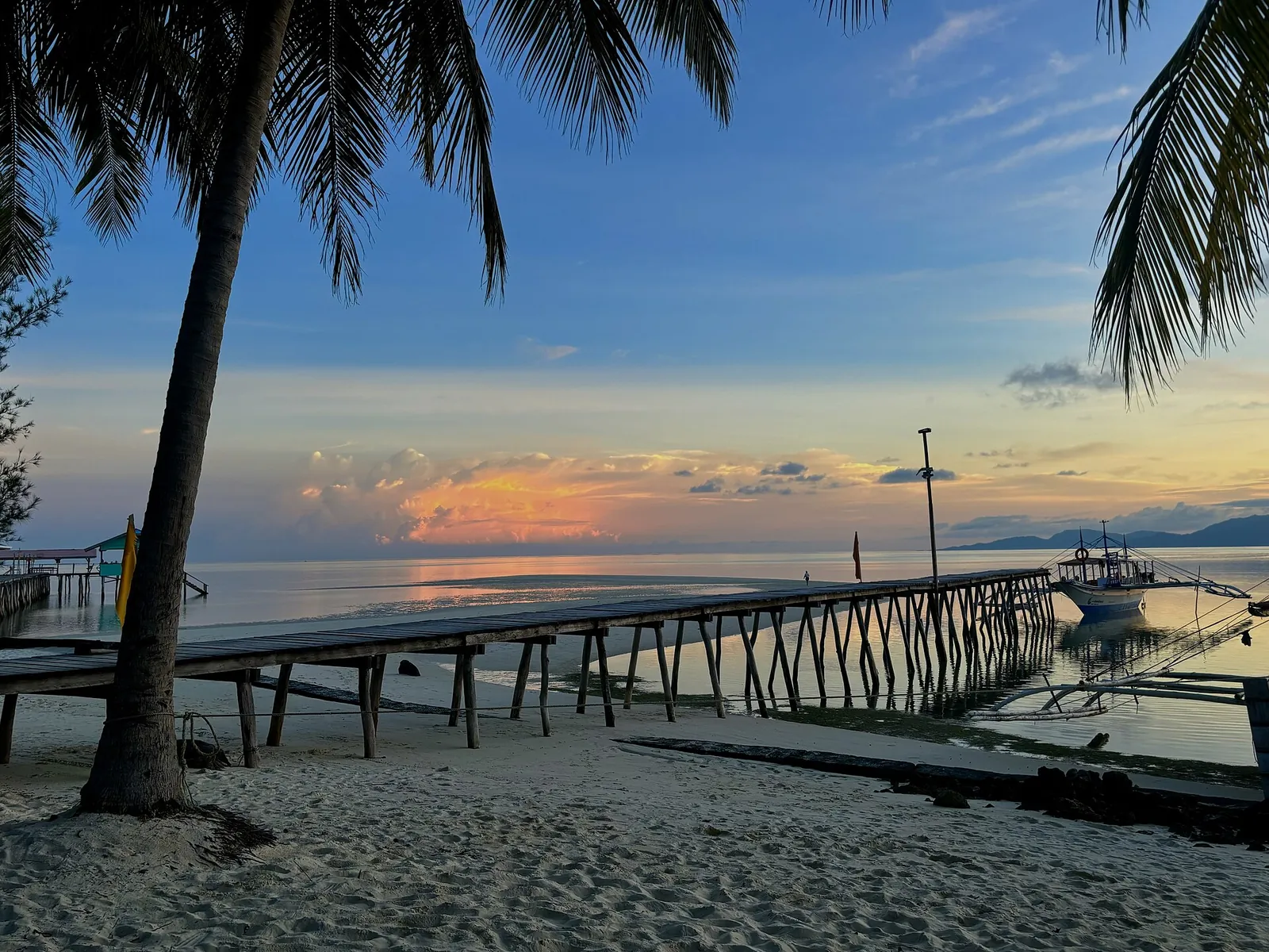 Palm silhouettes and a long wooden jetty at sunset on Onuk Island