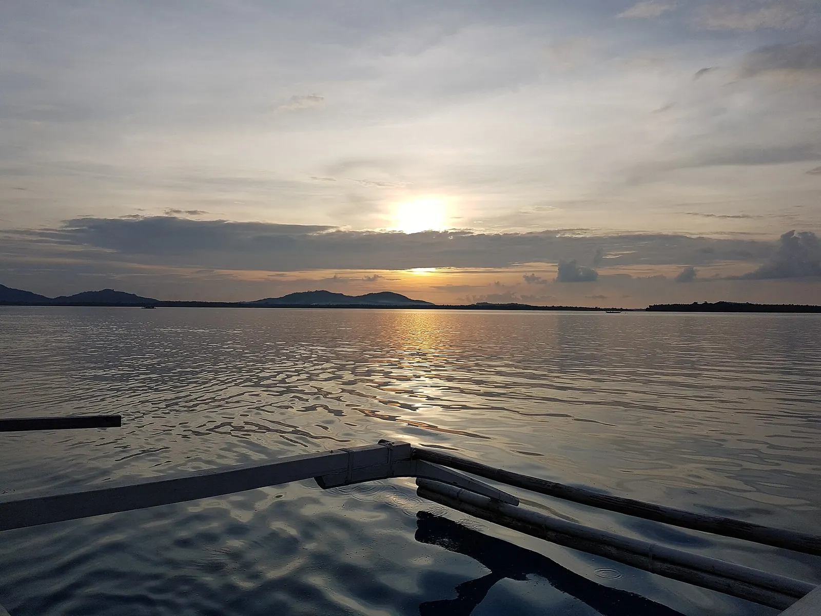 Sun setting across Balabac Strait beyond an outrigger boat beam