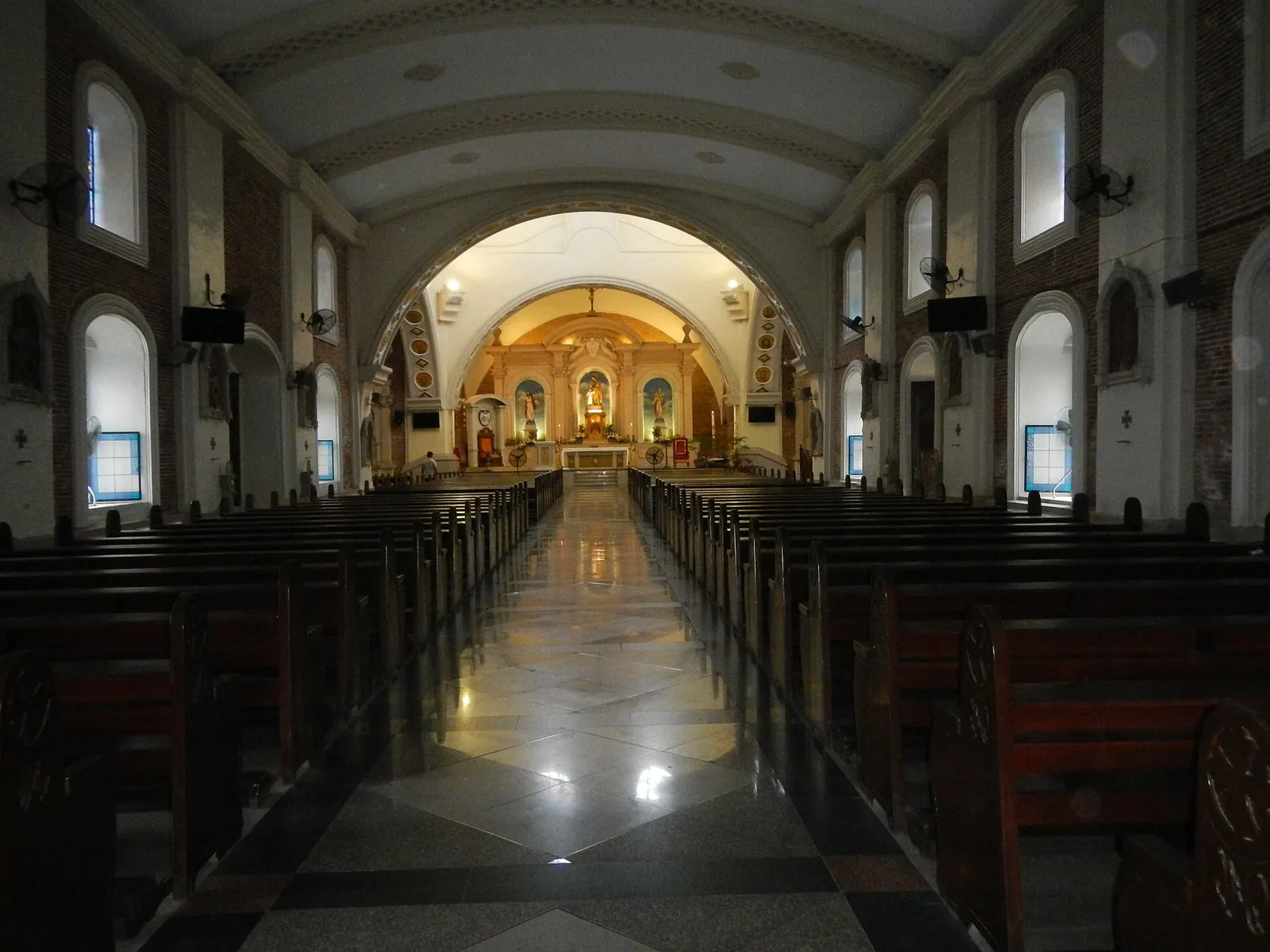 Long cathedral nave with wooden pews and a lit altar in Balanga