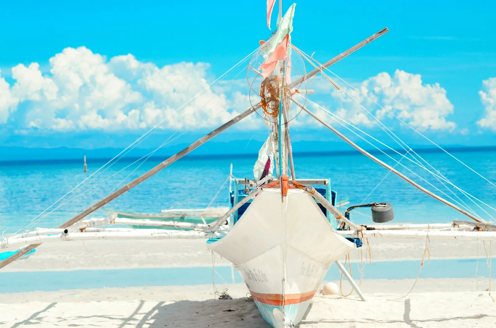 White outrigger boat resting on pale sand beside blue water on Bantayan Island